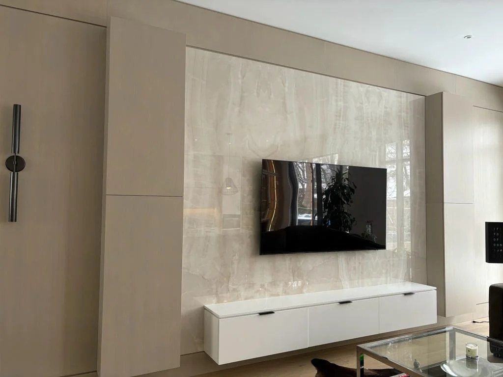Basement TV wall in onyx-look porcelain slab framed by oak-look wall panels, with a floating white media cabinet, by NewGen Renovations Vaughan