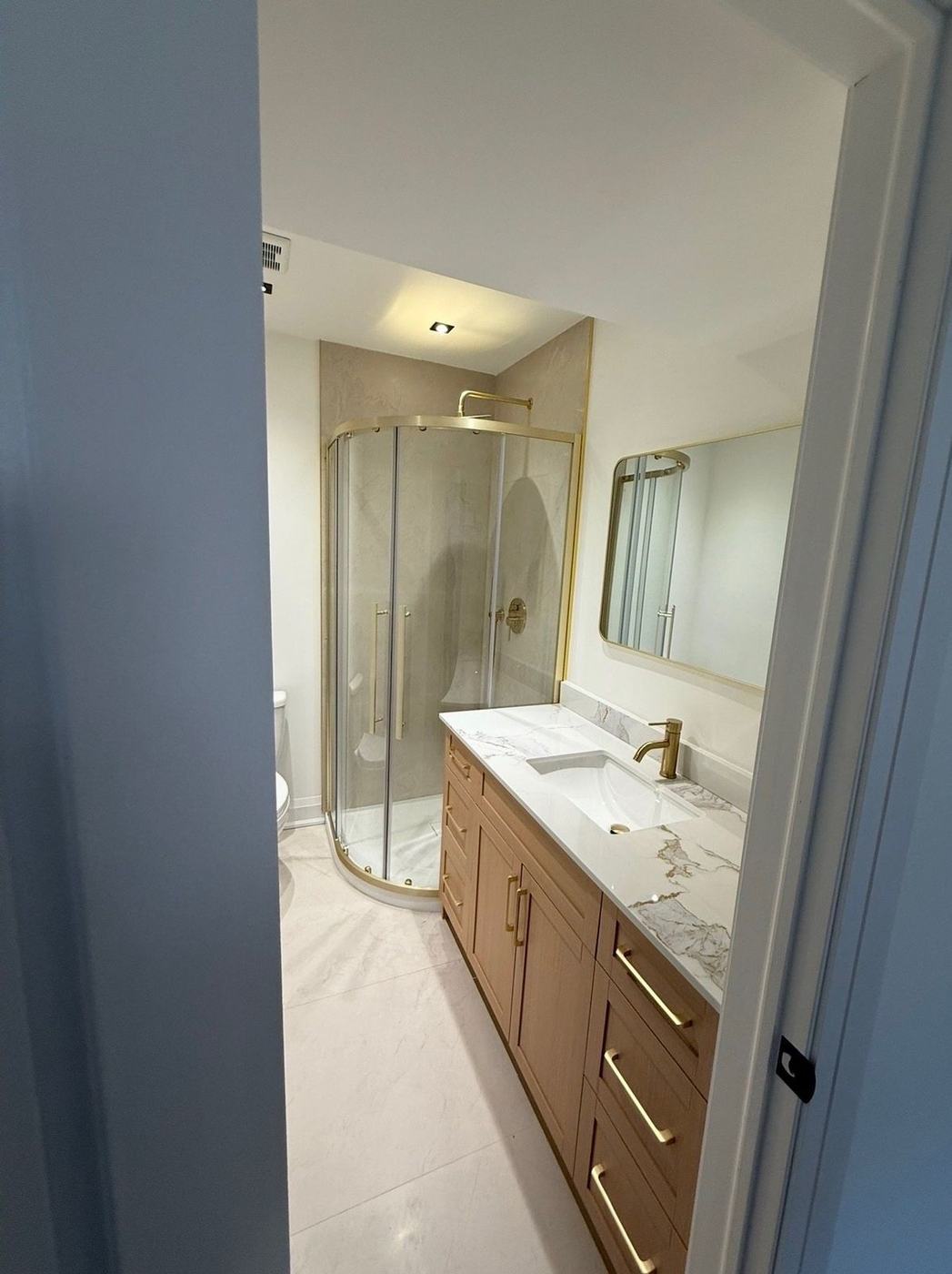 Bathroom with a round glass shower, brushed gold fixtures and a floating oak vanity in Maple, by NewGen Renovations Vaughan