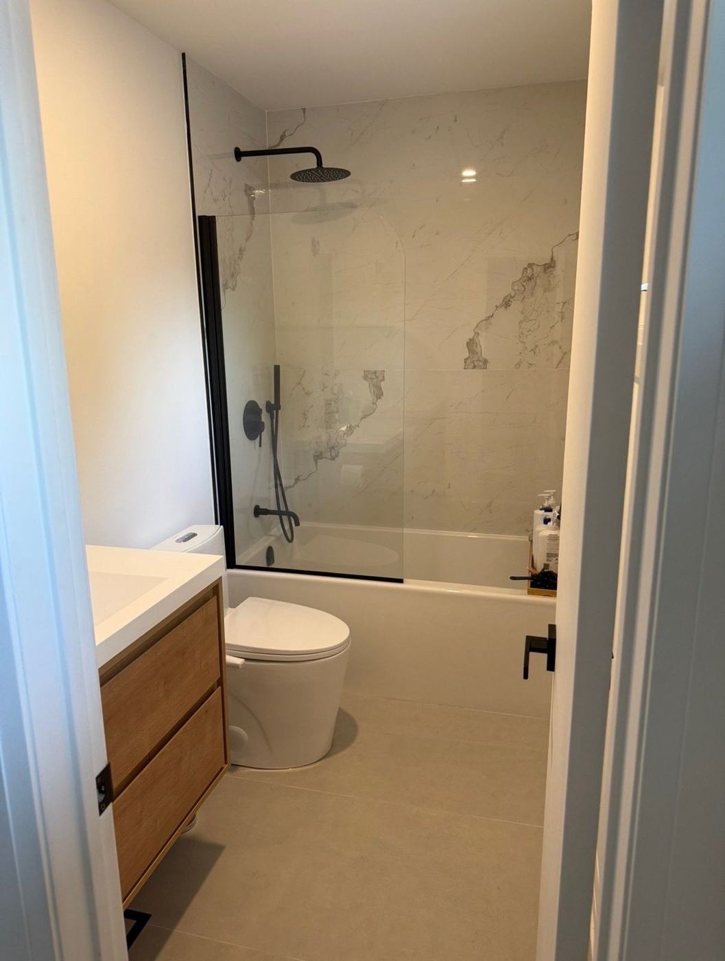 Bathroom with a glass splash panel over the tub, marble-look tile and a floating oak vanity in Maple, by NewGen Renovations Vaughan