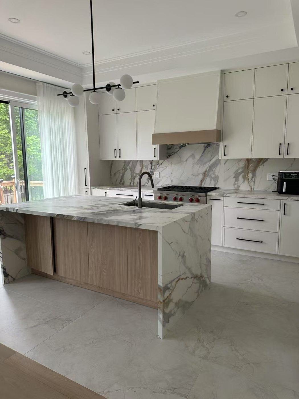 White kitchen with a marble-look waterfall island, slab backsplash and custom range hood, renovated by NewGen Renovations Vaughan