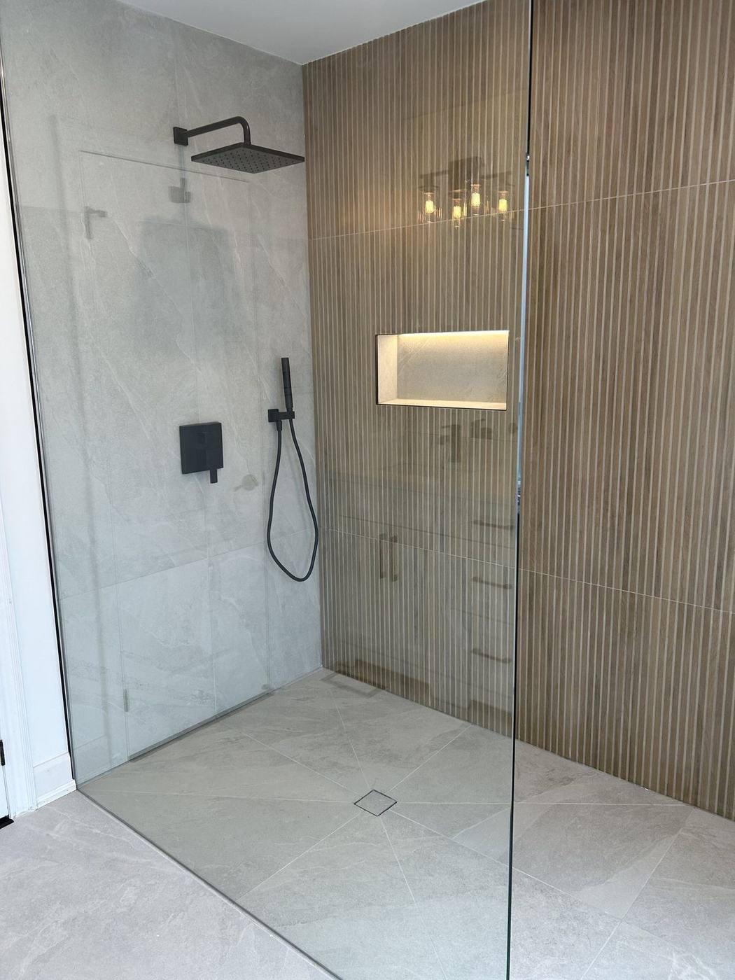 Curbless walk-in shower with matte black fixtures, lit niche and slatted wood-look tile after a bathroom renovation by NewGen Renovations Vaughan